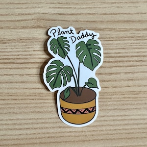 May include: A sticker featuring a potted plant with large green leaves. The pot is brown with a yellow band and a pink geometric pattern. The text "Plant Daddy" is written above the plant in a handwritten style.