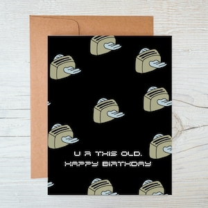 May include: A black card with a repeating pattern of toasters with wings. The text on the card reads "U R THIS OLD. HAPPY BIRTHDAY."