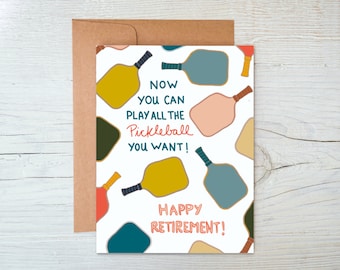 May include: A white card with a colourful illustration of pickleball paddles and the text "Now you can play all the pickleball you want! Happy Retirement!"