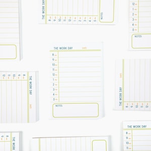 May include: White notepads with a green and blue design. Each notepad has a section for the time of day, labeled from 8 AM to 5 PM, and a space for notes. The text "THE WORK DAY" is printed on each notepad.