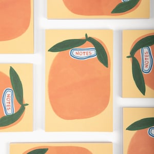 May include: A collection of notebooks with an orange illustration and green leaves on a yellow background. Each notebook has a blue and white label that says "NOTES". The notebooks are arranged in a grid pattern.