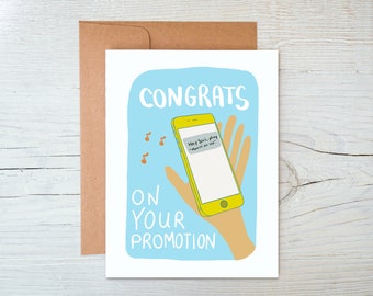 May include: A blue and white greeting card with a cartoon illustration of a hand holding a yellow smartphone. The phone screen displays a text message that says "Hey Siri, play "Movin' on Up."  The card reads "Congrats on your promotion."