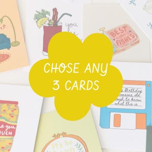May include: A selection of greeting cards with various illustrations, including a cocktail, a sardine can labeled "BEST FISHES," and a floppy disk. A yellow flower shape with the text "CHOSE ANY 3 CARDS" is in the center.