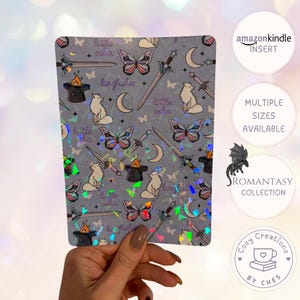 Può includere: Un adesivo rettangolare olografico a tema fantasy. Il design include farfalle, spade, lune, volpi e il testo "little osha" e "kingfisher". L'adesivo fa parte della "Romantasy Collection".