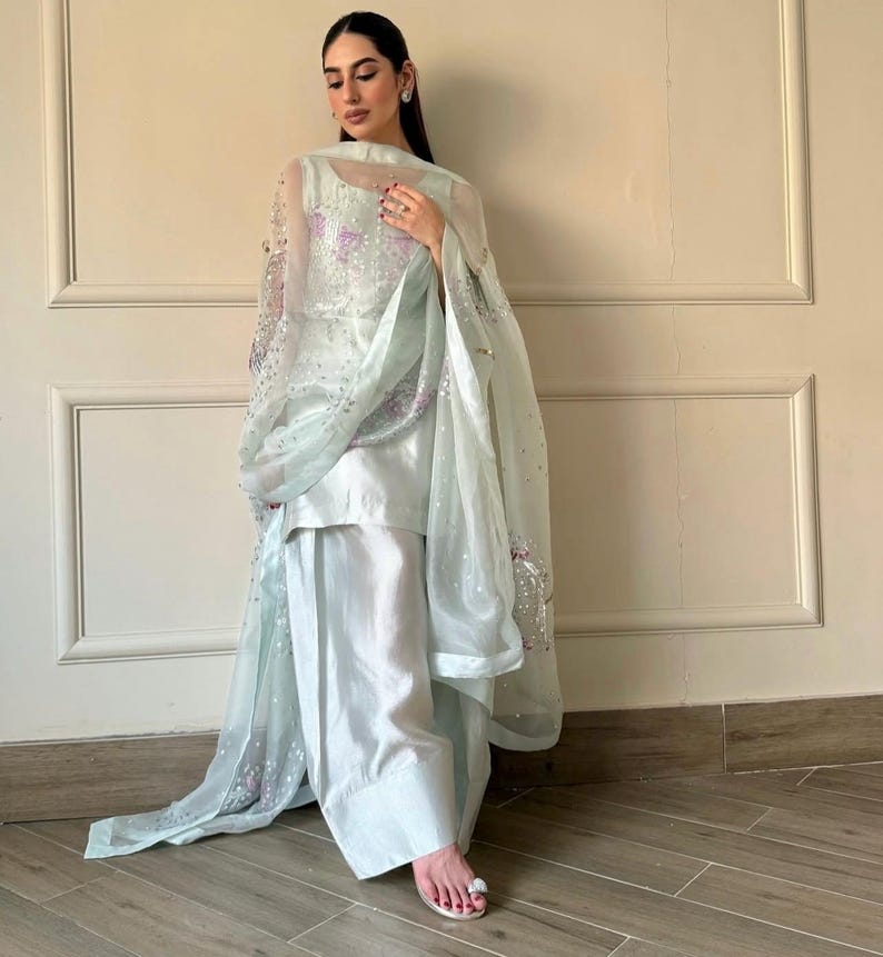 May include: A light blue, three-piece outfit featuring a tunic, wide-leg pants, and a sheer shawl. The shawl is adorned with sequins and floral embroidery. The outfit is made of a silky fabric and is suitable for formal occasions.
