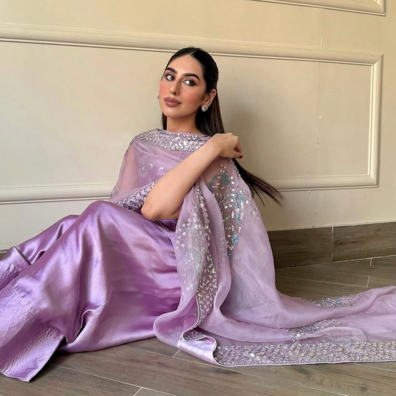 May include: A lilac-colored, flowing outfit with a matching sheer shawl. The shawl is adorned with silver sequins along the edges and scattered across the fabric. The outfit appears to be made of a satin-like material.