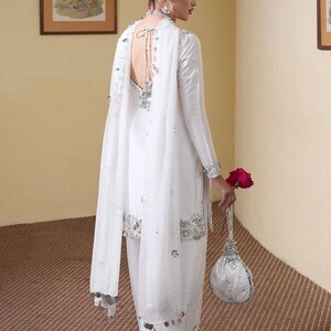Puede incluir: Un atuendo formal blanco con adornos plateados. El conjunto incluye una parte superior de manga larga, pantalones a juego y un chal transparente. Un peque&ntilde;o bolso decorativo y una rosa roja completan el look. Adecuado para ocasiones especiales.
