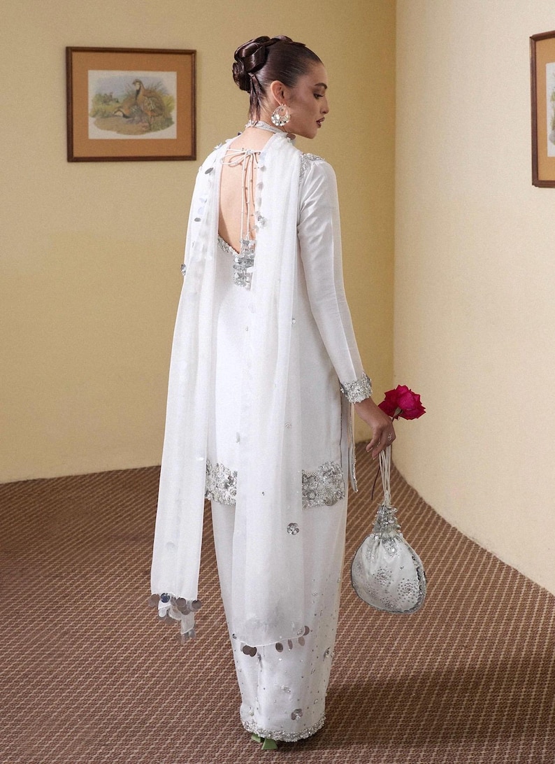 Puede incluir: Un atuendo formal blanco con adornos plateados. El conjunto incluye una parte superior de manga larga, pantalones a juego y un chal transparente. Un peque&ntilde;o bolso decorativo y una rosa roja completan el look. Adecuado para ocasiones especiales.
