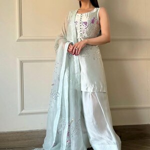 May include: A light blue formal outfit featuring a sleeveless top with sequin embellishments, matching wide-leg pants, and a sheer scarf. The outfit has a flowing, elegant design, suitable for special occasions.