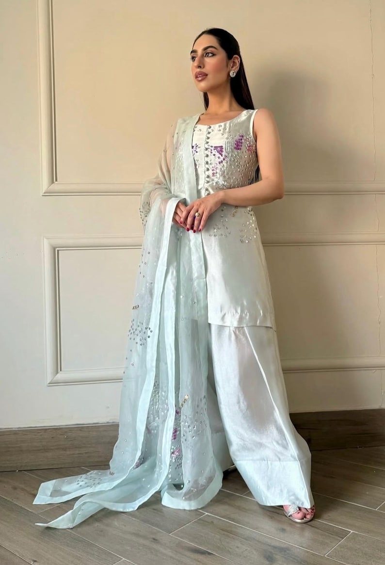 May include: A light blue formal outfit featuring a sleeveless top with sequin embellishments, matching wide-leg pants, and a sheer scarf. The outfit has a flowing, elegant design, suitable for special occasions.