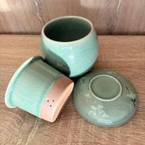 Può includere: Servizio da tè celadon in tre pezzi. Il set comprende una piccola tazza rotonda, un coperchio abbinato e una piccola tazza rotonda con base marrone chiaro. I pezzi hanno una glassa craquelé e un disegno di gru sul coperchio.