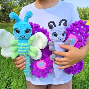 May include: Two plush butterfly toys made of soft yarn. The left toy is bright blue and lime green with white wings and large black eyes. The right toy is light purple with dark purple and pink patterned wings and large blue eyes.