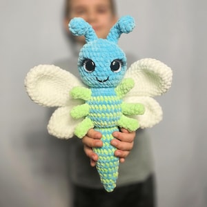 Op de afbeelding: Een gehaakt vlinder speelgoed met blauwe en groene strepen, witte vleugels en grote zwarte ogen.