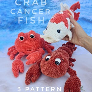 Pode incluir: Três animais de pelúcia de crochê: um caranguejo vermelho, uma lagosta vermelha e um peixe branco e vermelho. Os animais estão todos sentados em uma praia de areia branca. O texto "CRAB CANCER FISH" e "3 PATTERN" é visível na imagem.