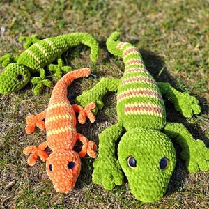 May include: Three crocheted lizard toys. One is green with yellow stripes, one is green with white stripes, and one is orange with yellow stripes.