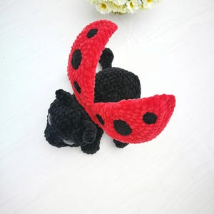 May include: A crocheted ladybug toy with black and red yarn. The ladybug has black spots on its red wings and is lying on its back with its wings open.