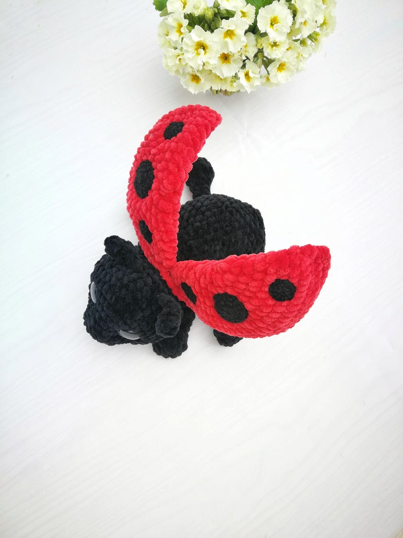 May include: A crocheted ladybug toy with black and red yarn. The ladybug has black spots on its red wings and is lying on its back with its wings open.