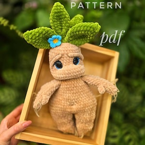 Pode incluir: Padrão de crochê para um brinquedo de pelúcia em forma de criatura vegetal com folhas verdes, corpo marrom e uma flor azul. O padrão está disponível para download em PDF. O texto "PATTERN pdf" é visível na imagem.