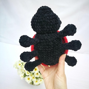May include: A black crocheted ladybug plush toy with red accents. The toy has six legs and a round body.