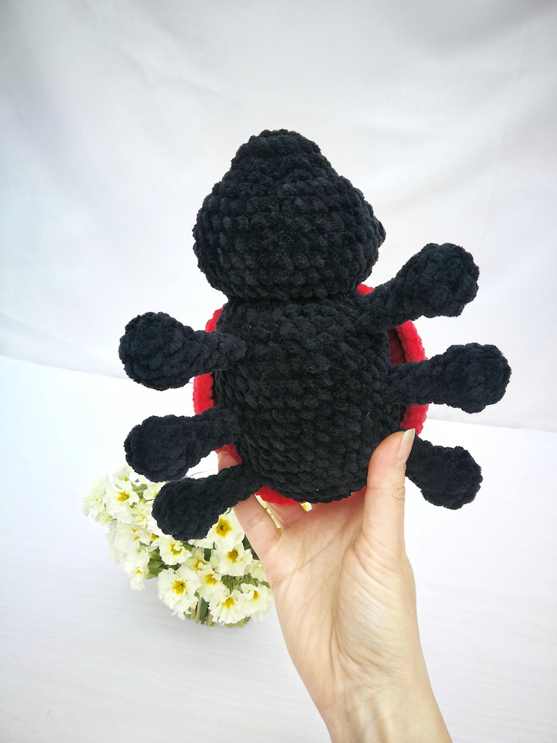 May include: A black crocheted ladybug plush toy with red accents. The toy has six legs and a round body.