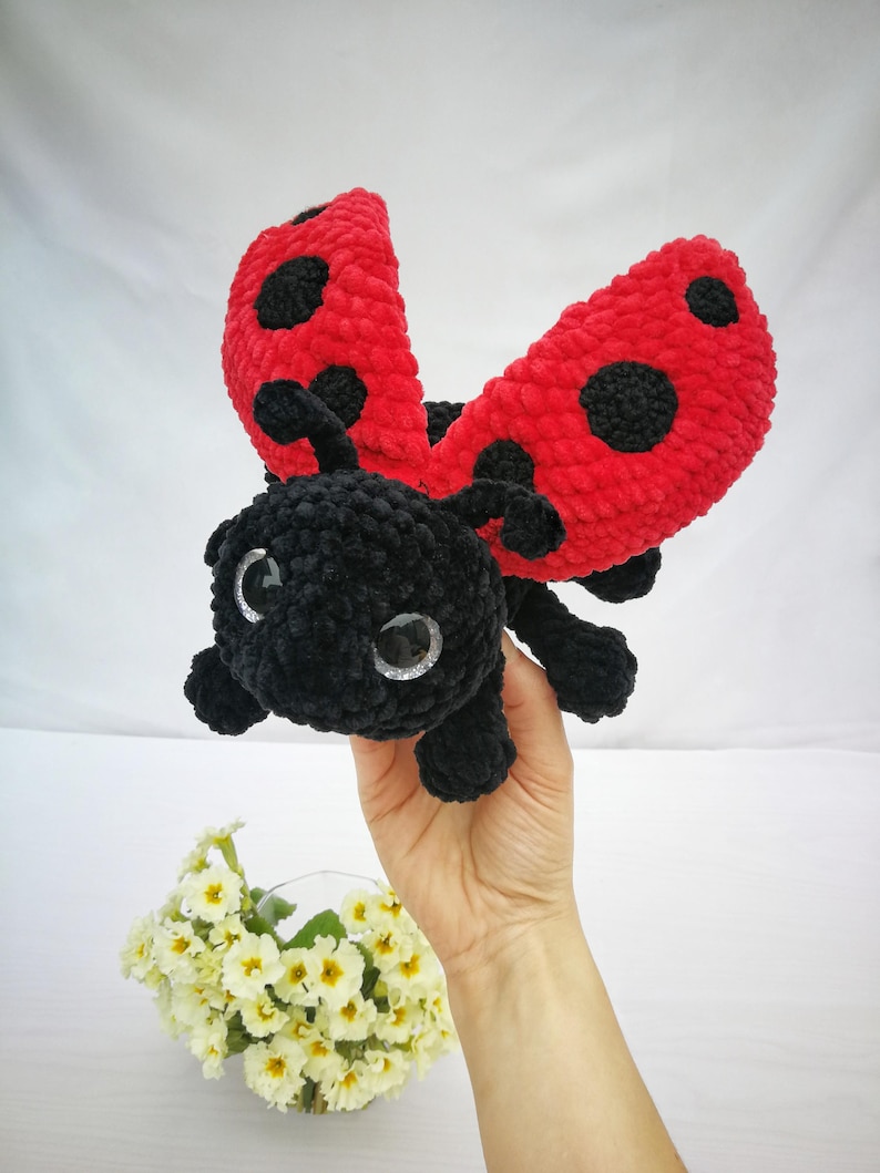 May include: A crocheted ladybug plush toy with black and red yarn. The ladybug has large black eyes and its wings are open.