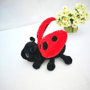 May include: A crocheted ladybug toy with black legs and a red body with black spots. The ladybug is lying on its back with its wings spread out.