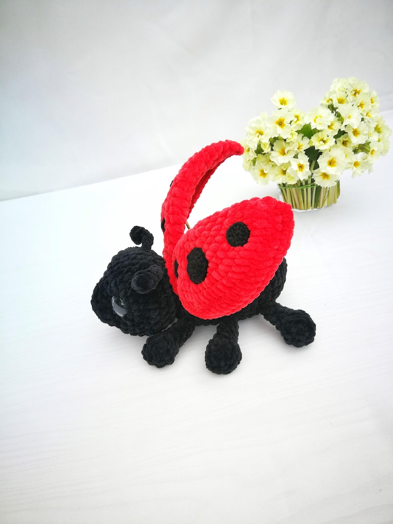 May include: A crocheted ladybug toy with black legs and a red body with black spots. The ladybug is lying on its back with its wings spread out.