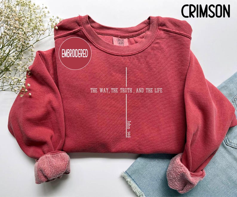 May include: Crimson-colored embroidered sweatshirt with the text "THE WAY, THE TRUTH, AND THE LIFE" and "John 14:6" in white. The sweatshirt has a crew neck and cuffed sleeves. The word "EMBROIDERED" is in a circle.