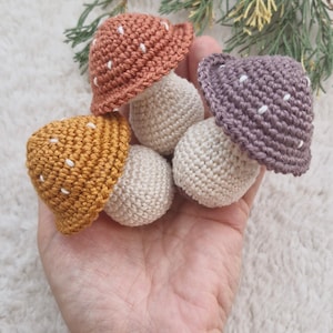 Puede incluir: Adornos de setas de ganchillo en tonos naranja, amarillo y morado con lunares blancos. Las setas tienen tallos beige. El texto "ENGLISH PATTERN" está en un rectángulo morado. Artesanía decorativa.