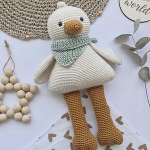 Puede incluir: Una muñeca de pato hecha a mano con cuerpo blanco, patas marrones y bufanda verde. El pato tiene un pico beige y un pequeño tocado blanco. La imagen también incluye un adorno de estrella de madera y un letrero que dice "hello world". El texto "ENGLISH PATTERN" está en la esquina superior izquierda.