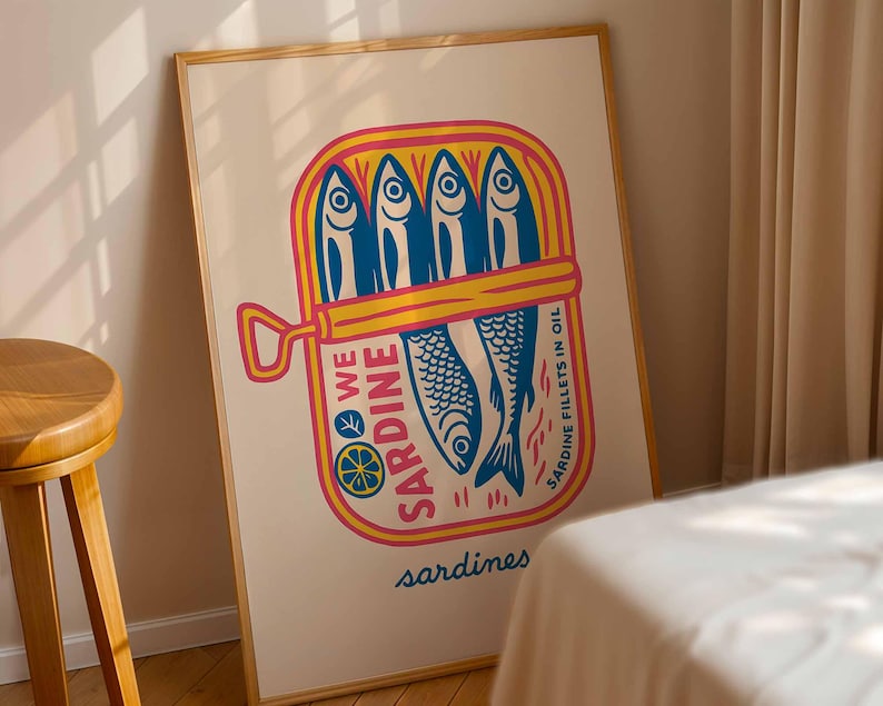 May include: A framed art print featuring a colorful illustration of a sardine can. The can is yellow and pink, with blue sardines inside. Text on the can reads "WE SARDINE" and "SARDINE FILLETS IN OIL". The word "sardines" is written at the bottom.