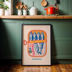 May include: A framed art print featuring a colorful illustration of a sardine can. The design includes blue fish, yellow and red accents, and the word "sardines" at the bottom. The artwork is displayed in a kitchen setting.