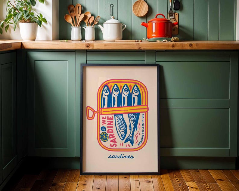 May include: A framed art print featuring a colorful illustration of a sardine can. The design includes blue fish, yellow and red accents, and the word "sardines" at the bottom. The artwork is displayed in a kitchen setting.