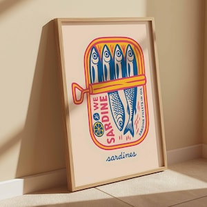 May include: A framed art print featuring a colorful illustration of a sardine can. The can is yellow and pink, with blue fish and the words "We Sardine" and "Sardine Fillets in Oil". The word "sardines" is written at the bottom.