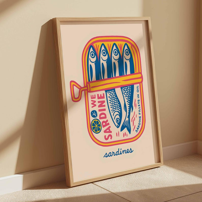 May include: A framed art print featuring a colorful illustration of a sardine can. The can is yellow and pink, with blue fish and the words "We Sardine" and "Sardine Fillets in Oil". The word "sardines" is written at the bottom.