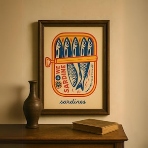 Retro fish print for vintage kitchen makeover or nautical bathroom wall art, ideal as a digital housewarming gift. May include: A framed print of a vintage style sardine can illustration. The can is yellow with red and blue accents. The text on the can reads 'SARDINE' and 'SARDINE FILLETS IN OIL'. The illustration features a group of blue sardines swimming in the can. The print is on a light beige background and the word 'sardines' is printed below the can illustration.