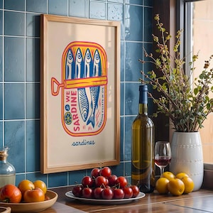 May include: A framed print featuring a colorful sardine can illustration with the text "WE SARDINE" and "SARDINE FILLETS IN OIL". The image is set in a kitchen with a bottle of wine, a glass of red wine, and a vase of flowers.