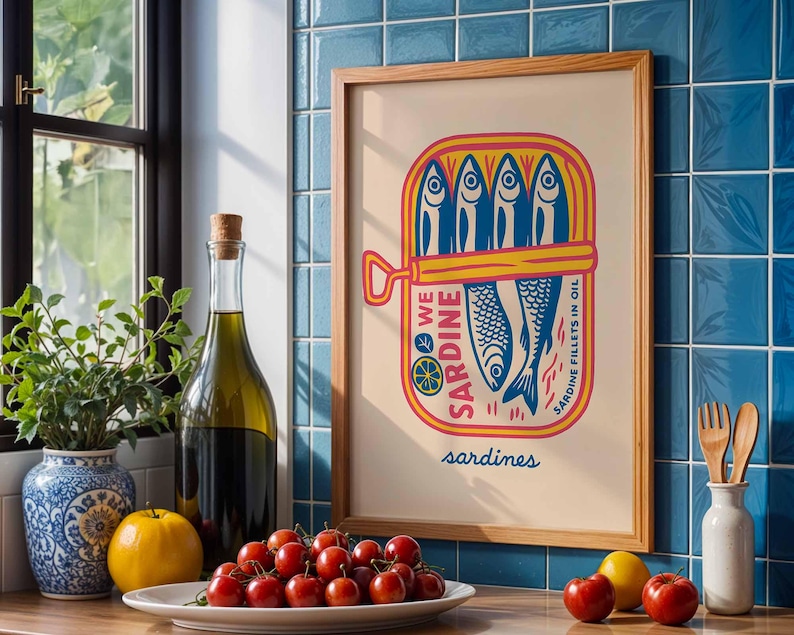 May include: A framed print featuring a colorful illustration of sardines in a can. The artwork includes the words "WE SARDINE" and "SARDINE FILLETS IN OIL". The print is displayed near a window, a bottle of olive oil, and fresh produce.