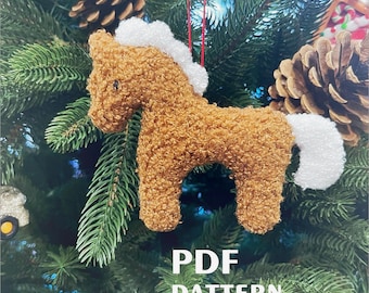 May include: A handmade, brown plush horse Christmas ornament with a white mane and tail. The ornament is hanging on a Christmas tree with pine needles and pine cones. The text "PDF PATTERN" is visible.