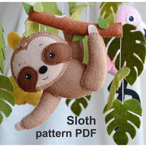 Puede incluir: Un perezoso marrón colgado de una rama con hojas verdes. El perezoso está hecho de fieltro y tiene una expresión linda y somnolienta. El texto "Sloth pattern PDF" está escrito debajo del perezoso.