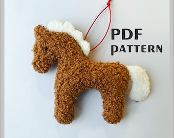 May include: A brown plush horse ornament with a white mane and tail, and a red string for hanging. The text "PDF PATTERN" is displayed in black. The horse is made of a curly, textured material.