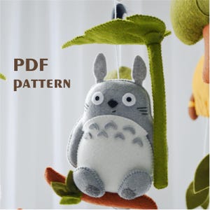 May include: A gray and white felt Totoro character with large eyes, sitting on a branch with a green leaf above it. The text "PDF PATTERN" is visible in the image.