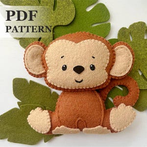Könnte beinhalten: PDF-Muster für ein Filz-Affenspielzeug. Der Affe ist braun mit einem beigefarbenen Gesicht, Ohren und Händen. Er hat schwarze Augen und eine schwarze Nase. Der Affe sitzt auf einem grünen Filzblatt.