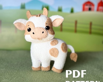 Peut inclure: Une vache en feutre blanc avec des taches brunes, debout sur une surface herbeuse verte. La vache a un visage amical avec des yeux noirs et un sourire cousu. Le texte "PDF PATTERN" est visible en bas de l'image.