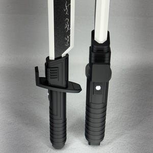 May include: Two black and white toy lightsabers. The blades are white, and one has a black section with a lightning bolt design. The handles are black with ribbed grips and button details. The lightsabers are displayed vertically.