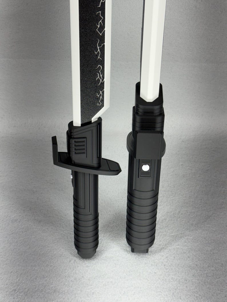 May include: Two black and white toy lightsabers. The blades are white, and one has a black section with a lightning bolt design. The handles are black with ribbed grips and button details. The lightsabers are displayed vertically.