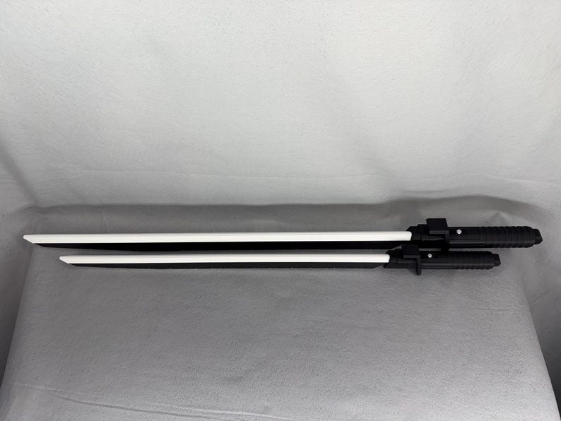 May include: Two black and white toy swords. The blades are white, and the handles are black with a textured grip. The swords are of different lengths, with the longer one measuring approximately 30 inches.