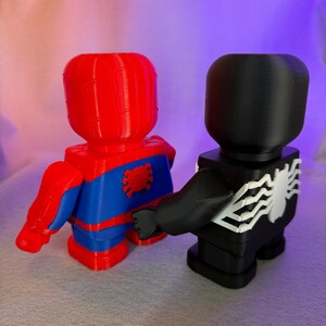 May include: Red and blue Spider-Man figurine standing next to a black Venom figurine. Both figurines are 3D printed and have a blocky design.