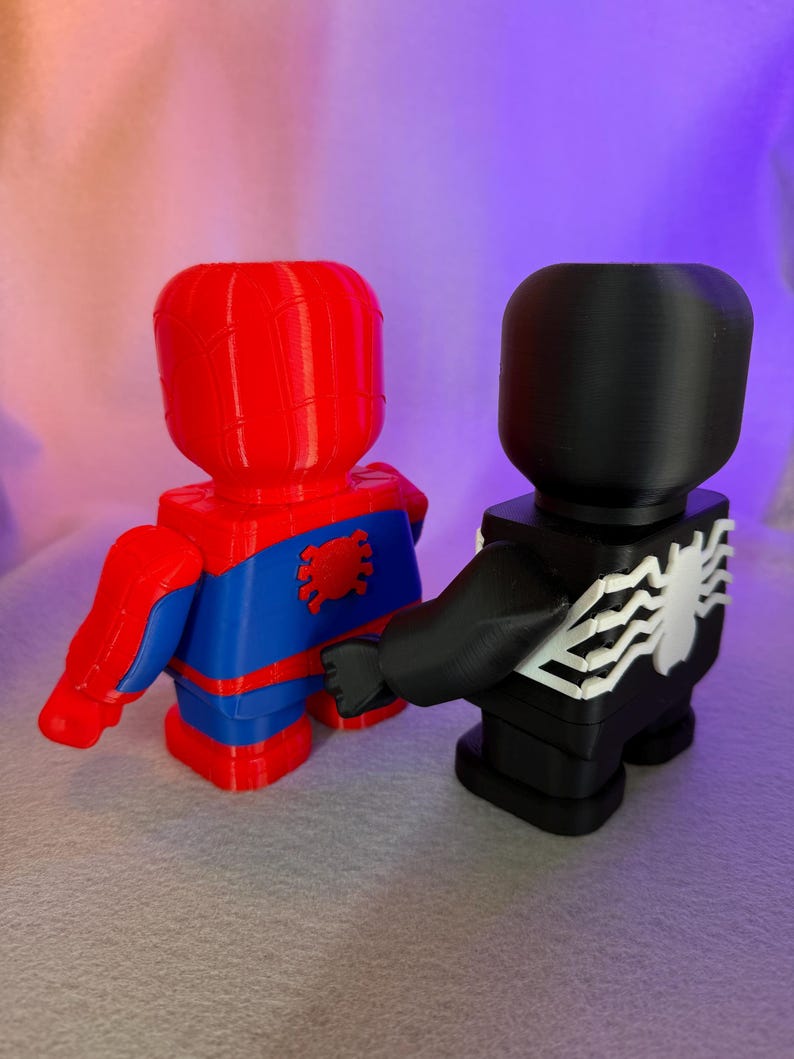 May include: Red and blue Spider-Man figurine standing next to a black Venom figurine. Both figurines are 3D printed and have a blocky design.
