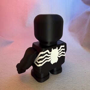 May include: Black and white 3D printed figurine of a superhero with a spider web design on the chest.